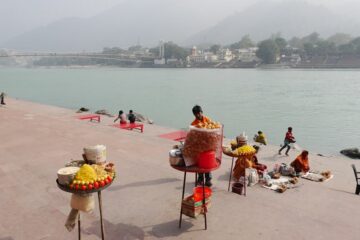 runder Verkaufstisch mit Opfergaben und Menschen am Ufer des Ganges