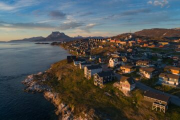 Häuser auf Hügelkuppe umgeben von Fjord und Berg