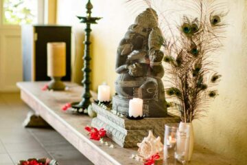 Ganesha Statue aus Stein mit Kerzen und Blumen daneben.