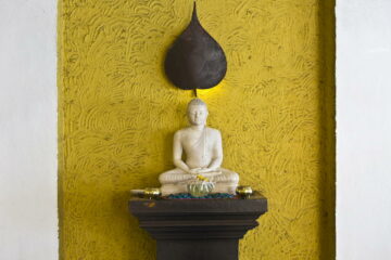 Buddha Statue auf einer kleinen Anrichte vor einer goldenen Wand.