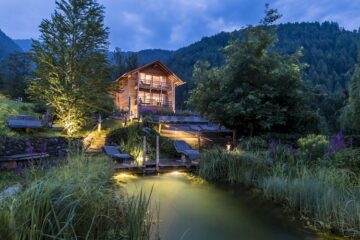 Großes Holzhaus inmitten der Natur in Südtirol, mit einem kleinen Teich bei Abendstimmung